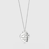 A silver heart-shaped pendant necklace with a key charm, featuring engraved text that reads 'PLEASE RETURN TO TIFFANY & CO. NEW YORK 925'.