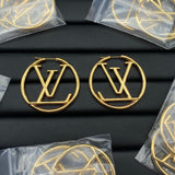 Gold hoop earrings with a logo on a black surface, surrounded by clear plastic bags.