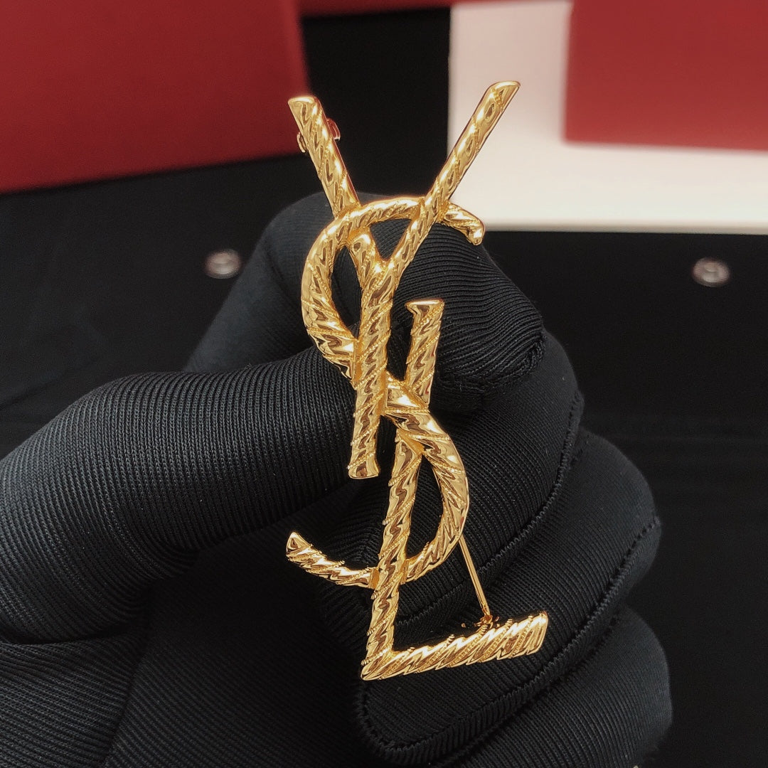 Gold YSL earrings held by a gloved hand with a red box in the background