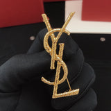 Gold YSL earrings held by a gloved hand with a red box in the background