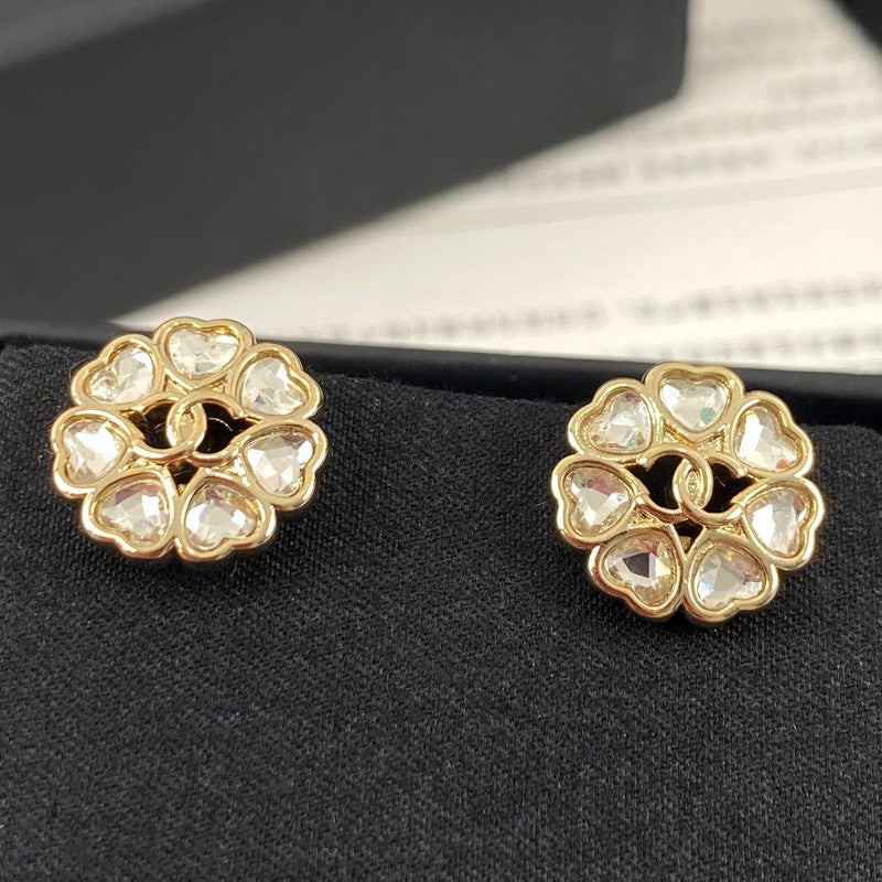 Gold earrings with heart-shaped gemstones on a black stand.
