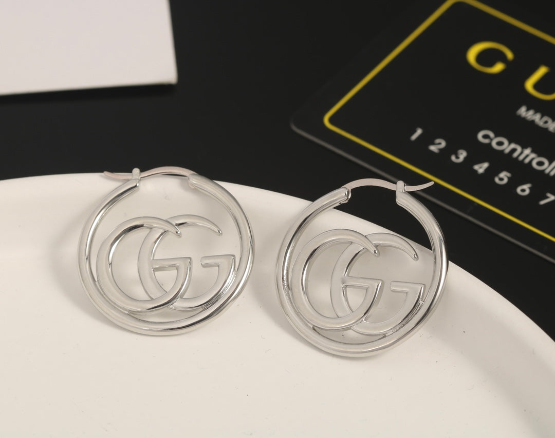 Silver hoop earrings with a logo on a white surface, Gucci card in the background